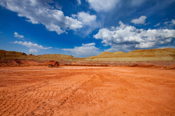 Bauxite clay quarry. Aluminium ore mining and transporting. Open-cut mine and orange Hitachi dump truck. On blue sky with white clouds background.