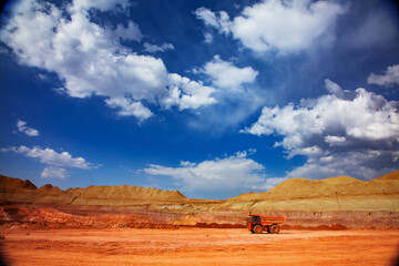 Aluminium ore mining and transporting. Bauxite clay quarry. Orange dump truck (quarry truck) Hitachi on red soil and blue sky with white clouds background.