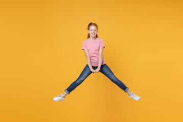Fototapeta na wymiar Full length children studio portrait of smiling little ginger redhead kid girl 12-13 years old wearing pink casual t-shirt posing jumping spreading legs isolated on bright yellow color background