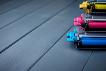 Magenta, cyan and yellow toner cartridges for color laser printers stacked on gray wooden background