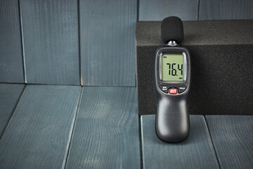 Digital sound level meter on acoustic foam in gray wooden space