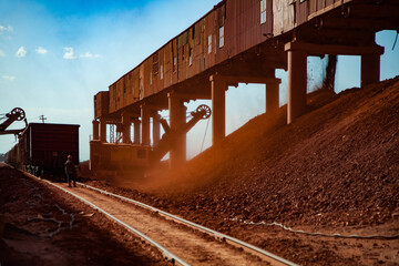 Fototapeta premium Bauxite clay open-cut mining. Loading and railway transporting terminal. Excavator load aluminium ore. Hopper car train on rails. Worker controlling process.