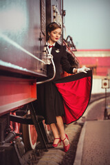 A young lady in vintage clothes standing on stairs of a historical retro train