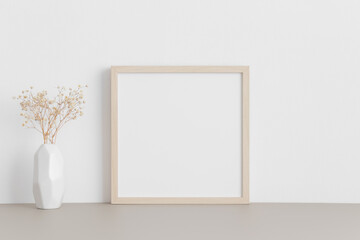 Square wooden frame mockup with a gypsophila in a vase on a beige table.