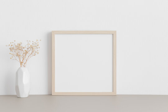 Square wooden frame mockup with a gypsophila in a vase on a beige table. © Snoflinga