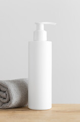 Obraz na płótnie Canvas White cosmetic shampoo dispenser bottle mockup with a towel on a wooden table.