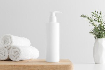 Obraz na płótnie Canvas White cosmetic shampoo dispenser bottle mockup with towels and a rosemary on a wooden table.