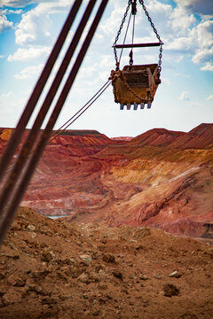 Aluminium ore quarry. Red bauxite clay open-cut mining. Walking dragline excavator bucket on cable of mast at work. Blue sky, clouds.