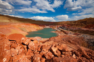 Green quarry lake in bauxite mine. On blue sky with clouds in summer day. Aluminium ore open-cut (open cast, open-pit) mining in quarry.
