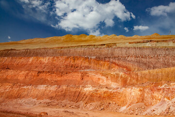 Aluminium ore quarry color layers. Bauxite clay open-cut mining. Texture of mineral cutting with excavator bucket. Blue sky with clouds background.