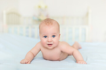 Cute adorable caucasian little 5 month old infant baby boy lying on tummy at nursery bed room having fun playing and smiling. Happy healthy newborn child concept. Funny toddler kid closeup portrait