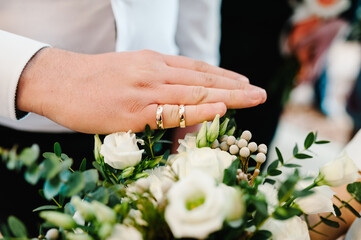 Obraz na płótnie Canvas Two golden wedding rings on the fingers against the background of a bouquet of flowers in their hands.