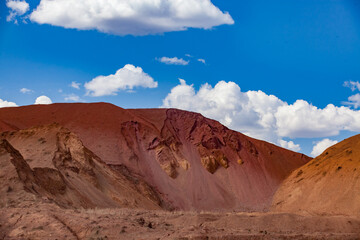 Aluminium ore quarry. Bauxite clay open cast (open cut) mining. Big yellow heaps of empty rocks. Blue sky with clouds.