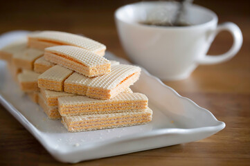 Wafers in white dish and black coffee in white cup on brown wooden table