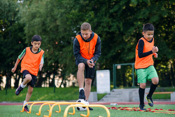 Two school boys are running ladder drills on the turf during football summer camp. Intense soccer...