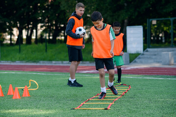 Two school boys are running ladder drills on the turf during football summer camp. Intense soccer training with coach.