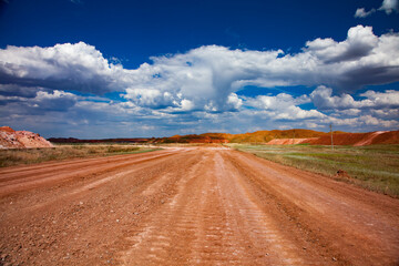 Fototapeta na wymiar Colorful landscape of bauxite mine (aluminium ore quarry). Orange soil and road and green grass. Blue sky with clouds.