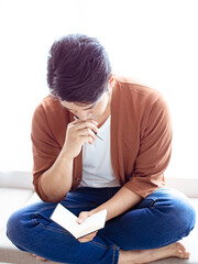 Cross-legged young asian man writing in notebook.