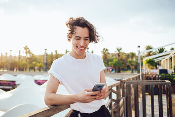 Cheerful Millennial tourist enjoying smartphone communication during influence blogging on travel website, prosperous hipster guy reading funny publication in social networks using 4g on cellphone