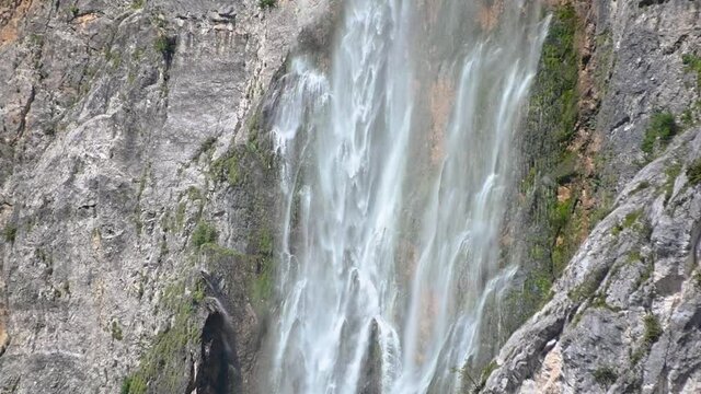 Slow motion waterfall Boka, Slovenia. Water gently flowing down the rocks. Moss growing under waterfall. Tilt down, close up