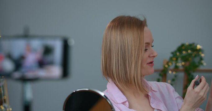 Beautiful girl talking and applying and demonstrating lipstick on her hand while recording video for her beauty vlog. Woman vloger making new episode about make up for subscribers.