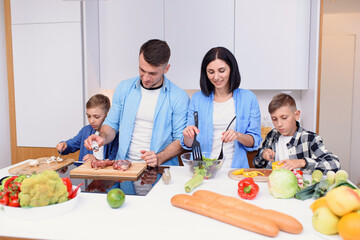 Mom, dad and two sons preparing together healthy breakfast with meat and vegetables on cozy kitchen at dining table.