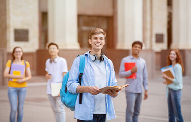 Cheerful Millennial Guy Standing Among Multiethnic Students Near University Outdoor