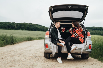 Young Beautiful Couple Sitting in the Car Trunk and Enjoying the Roadtrip, Picnic Concept