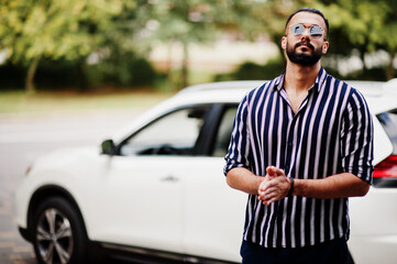 Successful arab man wear in striped shirt and sunglasses pose near his white suv car. Stylish arabian men in transport.