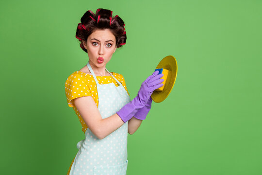 Photo of amazed cute girl wash plate sponger violet latex gloves impressed wear hair rollers vintage skirt isolated over green color background