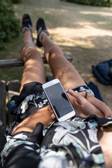 Young woman holds phone with a black screen and plays a game looking over her shoulder while she is lying down in the park