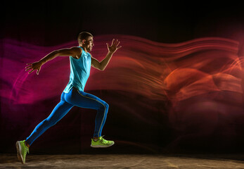 Professional male runner training isolated on black studio background in mixed light. Man in...