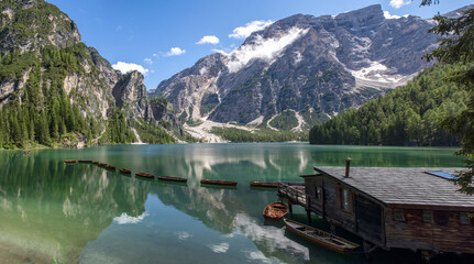 Fototapeta na wymiar Panoramic view of the Lake Braies, Pragser Wildsee, lake in the Prags Dolomites, South Tyrol, Italy. Detail of rowboats moored in line on pristine water near a wooden cabin and mountains 