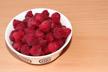 Ripe raspberries in a white plate on a beige wooden background.