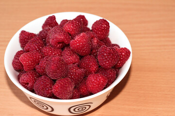 Ripe raspberries in a white plate on a beige wooden background.