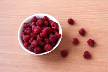 Ripe raspberries in a white plate on a beige wooden background.