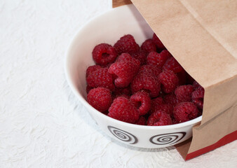 Food delivery. Raspberries in a white plate on a light background.