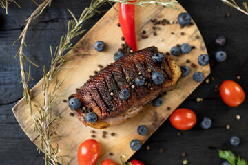 Goose breast Christmas roast with blueberries, tomatoes, red peppers and rosemary served on a wooden board