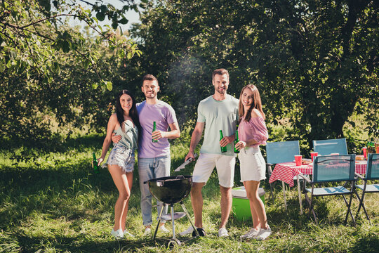 Full body photo of four people couple girl boys student have fun summer vacation garden cook grill meat sausages drink hold bottle beer under green tree outside