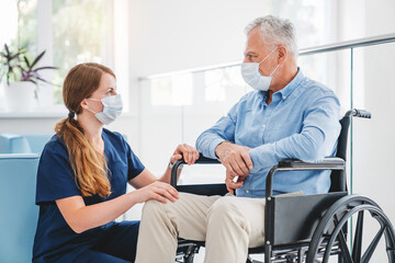 Young nurse taking care of mature male patient on wheelchair in hospital. Caucasian woman and old...