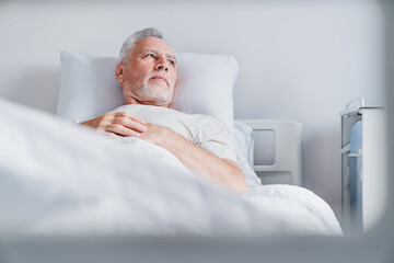 Mature caucasian male patient resting while lying on bed in moderm hospital ward room