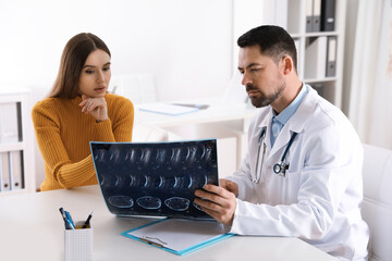Orthopedist showing X-ray picture to patient at table in clinic