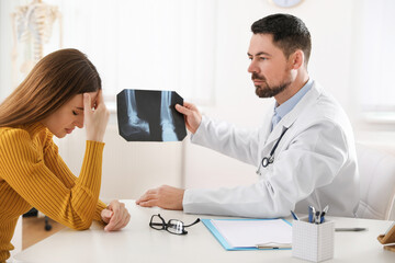 Orthopedist showing X-ray picture to patient at table in clinic