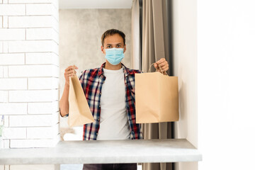 Delivery man holding a paper bag with food. Man delivering food in disposable paper bag to customer home with facemask. Delivery in time of coronavirus
