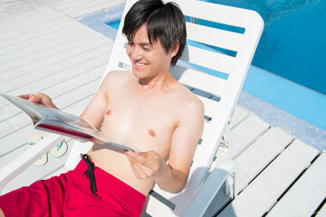 サマーベッドに座って雑誌を読む水着姿の男性