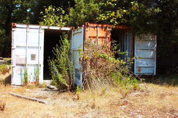 large empty containers made of rusted steel abandoned among dirt in a clearing of a wood