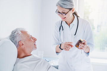 Asian female middle aged doctor in white medical coat holding bottle of pills, offering medicine to her old patient and smiling