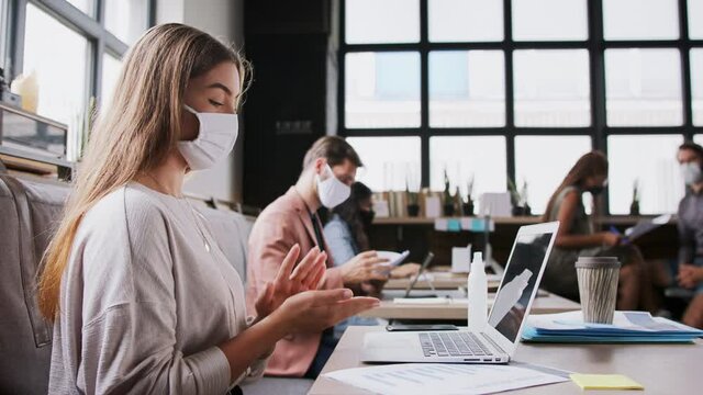 Portrait of young businesspeople with face masks working indoors in office, disinfecting laptop.