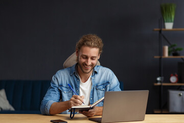 Studying online,online courses.Business concept.Young handsome curly smiling man with long hair studying in home with laptop.Business portrait of handsome manager sitting at workplace.