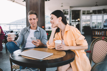 Cheerful coworkers enjoying coffee and using smartphone